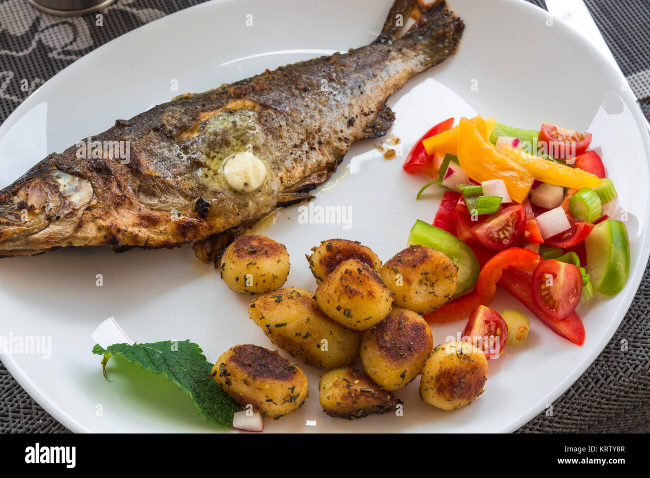 Gebratene Forelle mit weißem Teller mit Zitronen und Bratkartoffel. Stockfoto