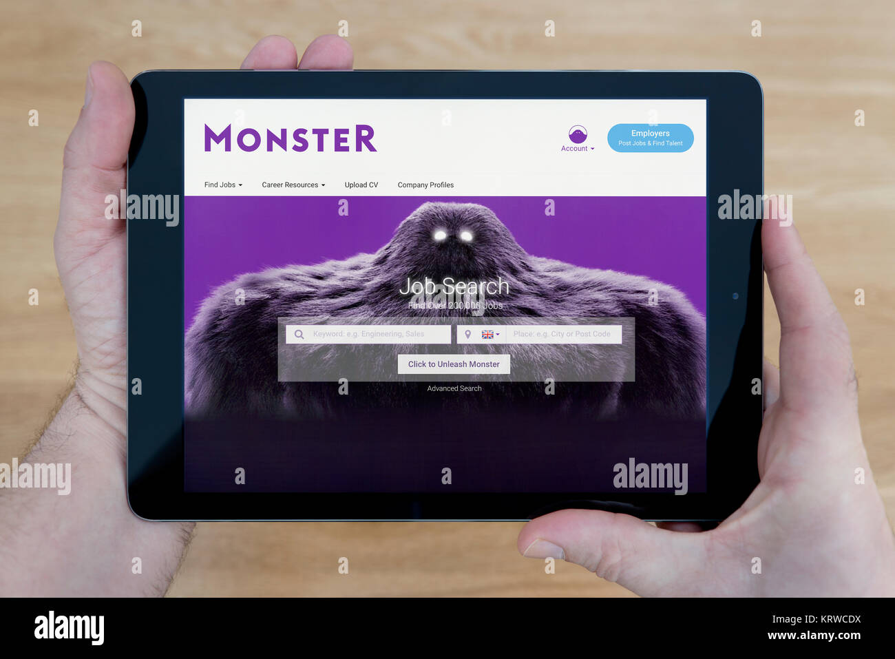 Ein Mann sieht das Monster Website auf seinem iPad tablet device, Schuß gegen einen hölzernen Tisch top Hintergrund (nur redaktionelle Nutzung) Stockfoto