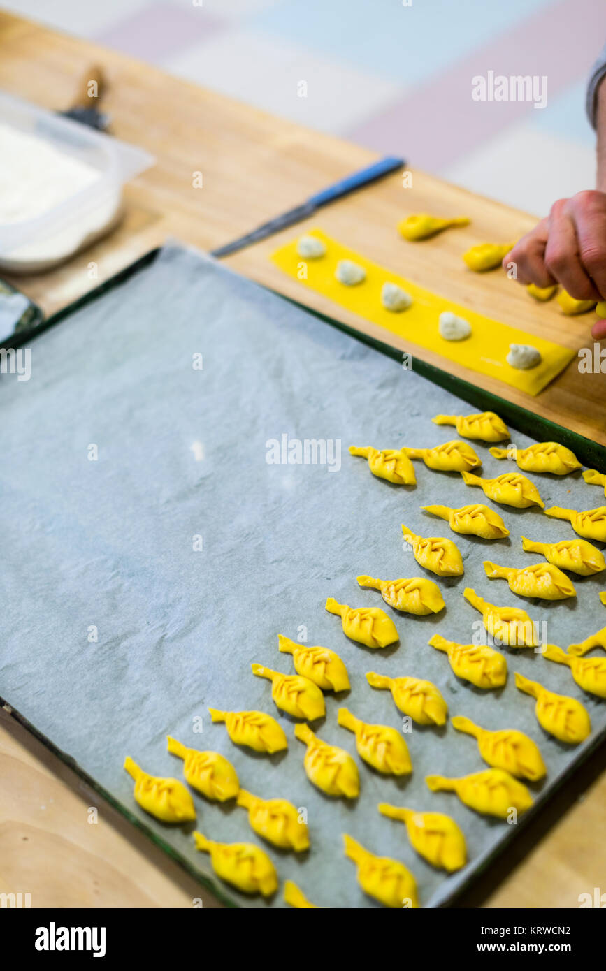 Professionelle ältere 70er Jahre 80er Jahre Dame, die handgemachte Ricotta Tortelli con la coda gefüllte Pasta in einer professionellen Küche mit frischen Zutaten zubereitet. Stockfoto