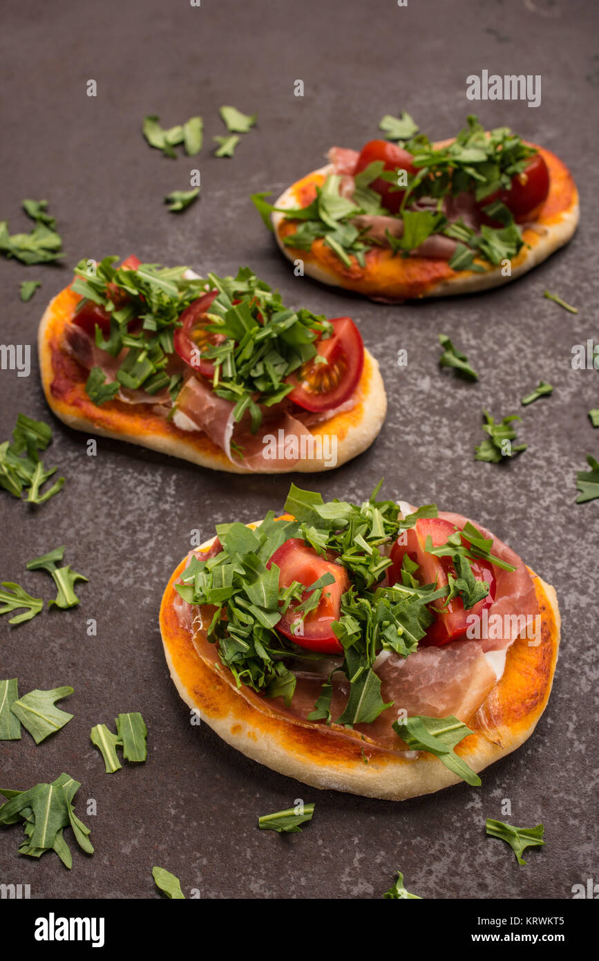 Mini Pizza mit Rucola, Tomate, Mozzarella und Schinken Stockfoto