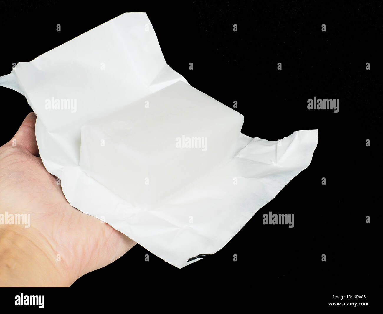 Unwrapped Block von Kokosfett in Aluminium Papier von einer Person gehalten wird, in Richtung Schwarz Stockfoto