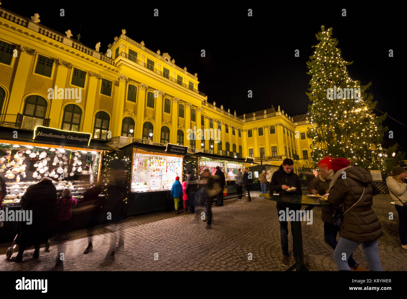 Traditioneller Weihnachtsmarkt mit beleuchteten Schloss Schönbrunn und Lichterketten geschmückten Weihnachtsbaum in der Dämmerung, Touristen und Menschen in festlicher Stimmung Stockfoto
