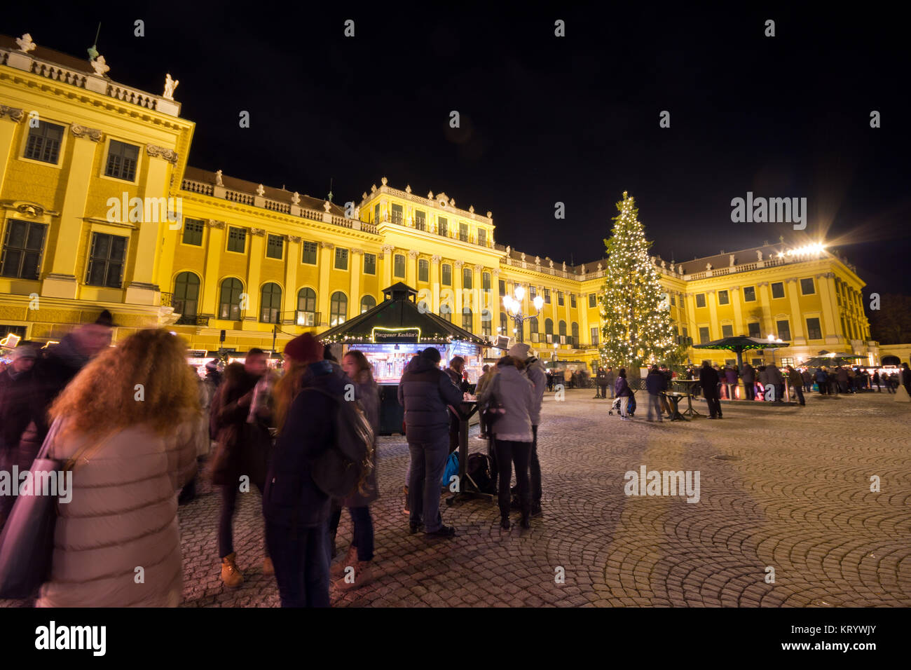 Traditioneller Weihnachtsmarkt mit beleuchteten Schloss Schönbrunn und Lichterketten geschmückten Weihnachtsbaum in der Dämmerung, Touristen und Menschen in festlicher Stimmung Stockfoto