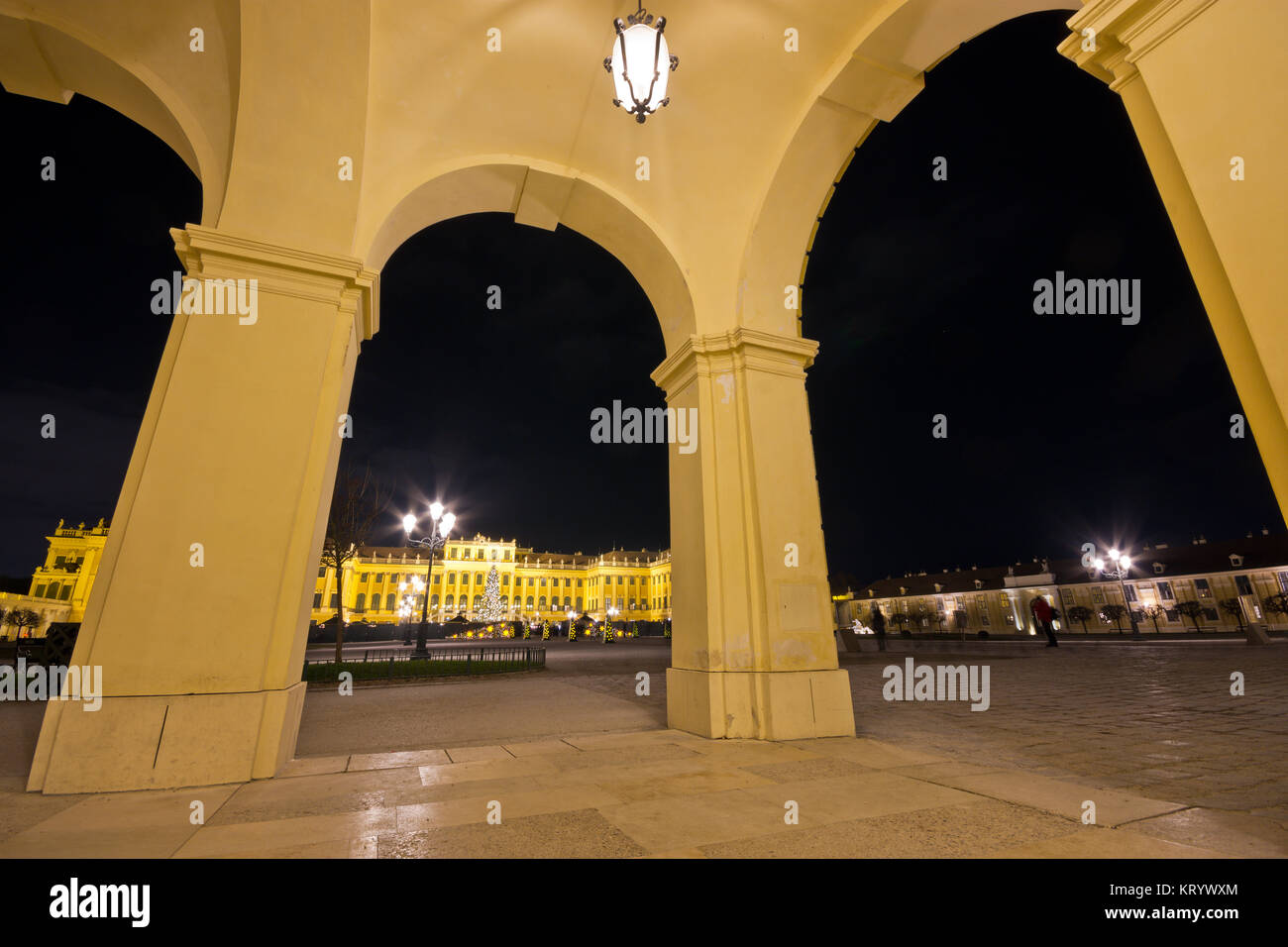 Blick auf das beleuchtete Schloss Schönbrunn nachts durch Bögen auf Säulen. Stockfoto