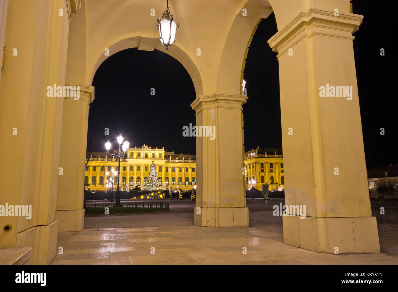 Blick auf das beleuchtete Schloss Schönbrunn nachts durch Bögen auf Säulen. Stockfoto