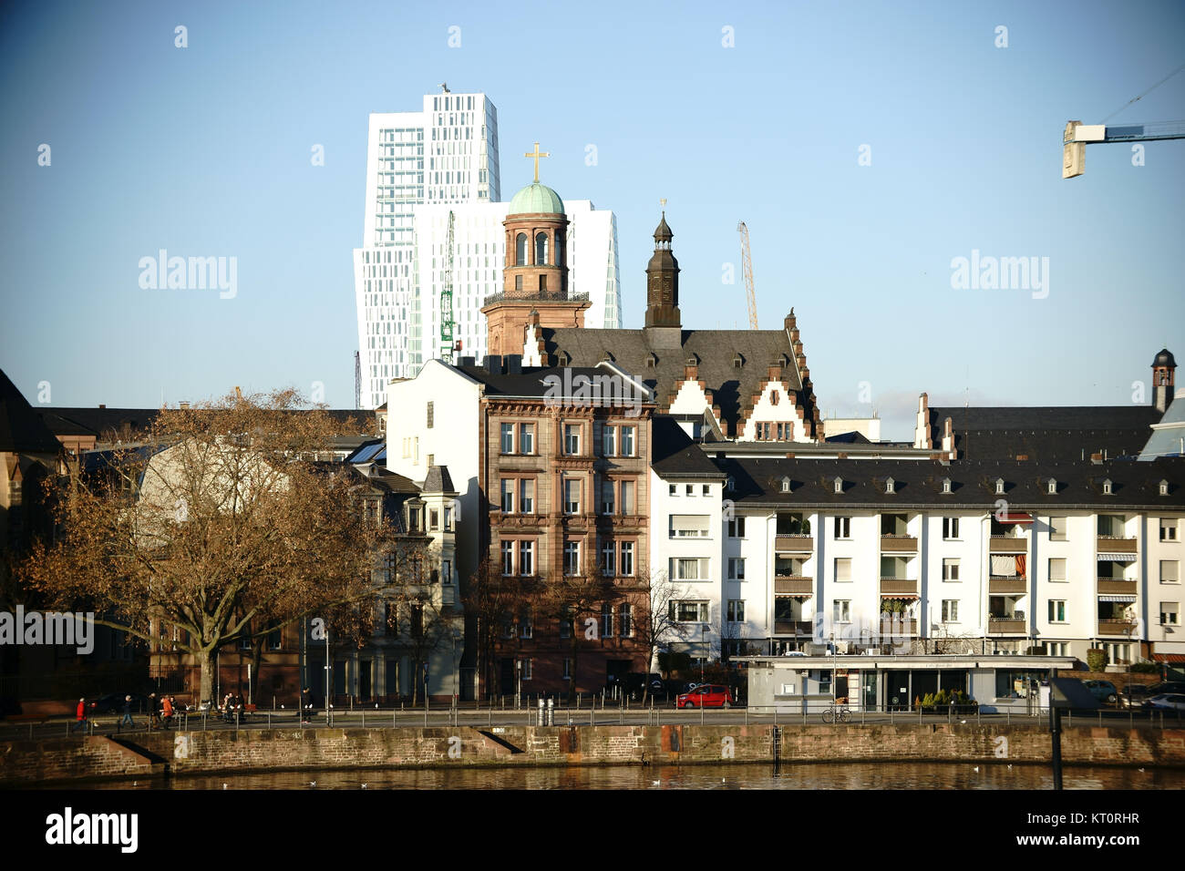 Der Turm der Liebfrauenkirche und andere Gebäudetürme hinter Wohnhäusern am Mainufer in Frankfurt. Stockfoto