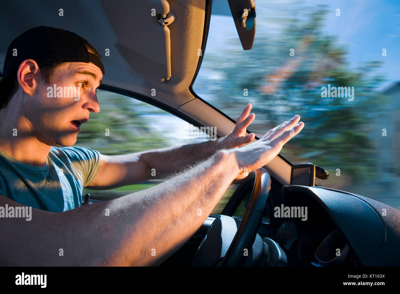 Seitliche Ansicht des jungen Autofahrers am Lenkrad vom Licht entgegenkommender Fahrzeuge geblendet und mit schockiertem Gesichtsausdruck. Stockfoto