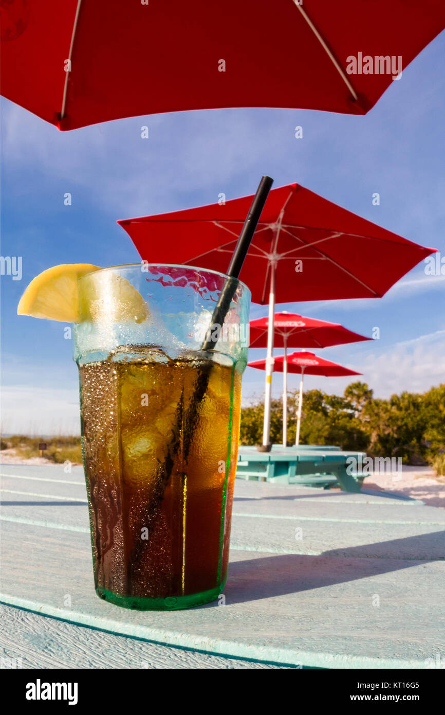 Glas aus Eis kalten Eistee mit Zitrone sitzen am Tisch unter Red Sonnenschirme am South Beach Bar & Grill am Gasparilla Island, Florida Stockfoto