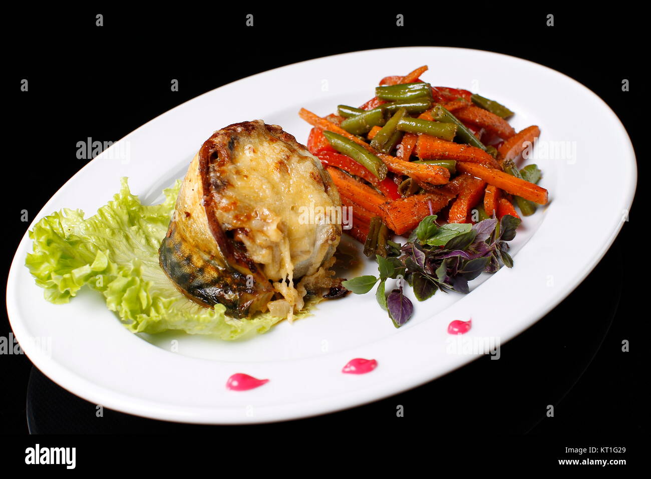 Auf einem weißen Teller Fisch frittierte Makrele in Käse, gekochtes Gemüse. Grüne Bohnen, Möhren, Basilikum, Salat., auf einem schwarzen Hintergrund. Gebratene Makrele Stockfoto