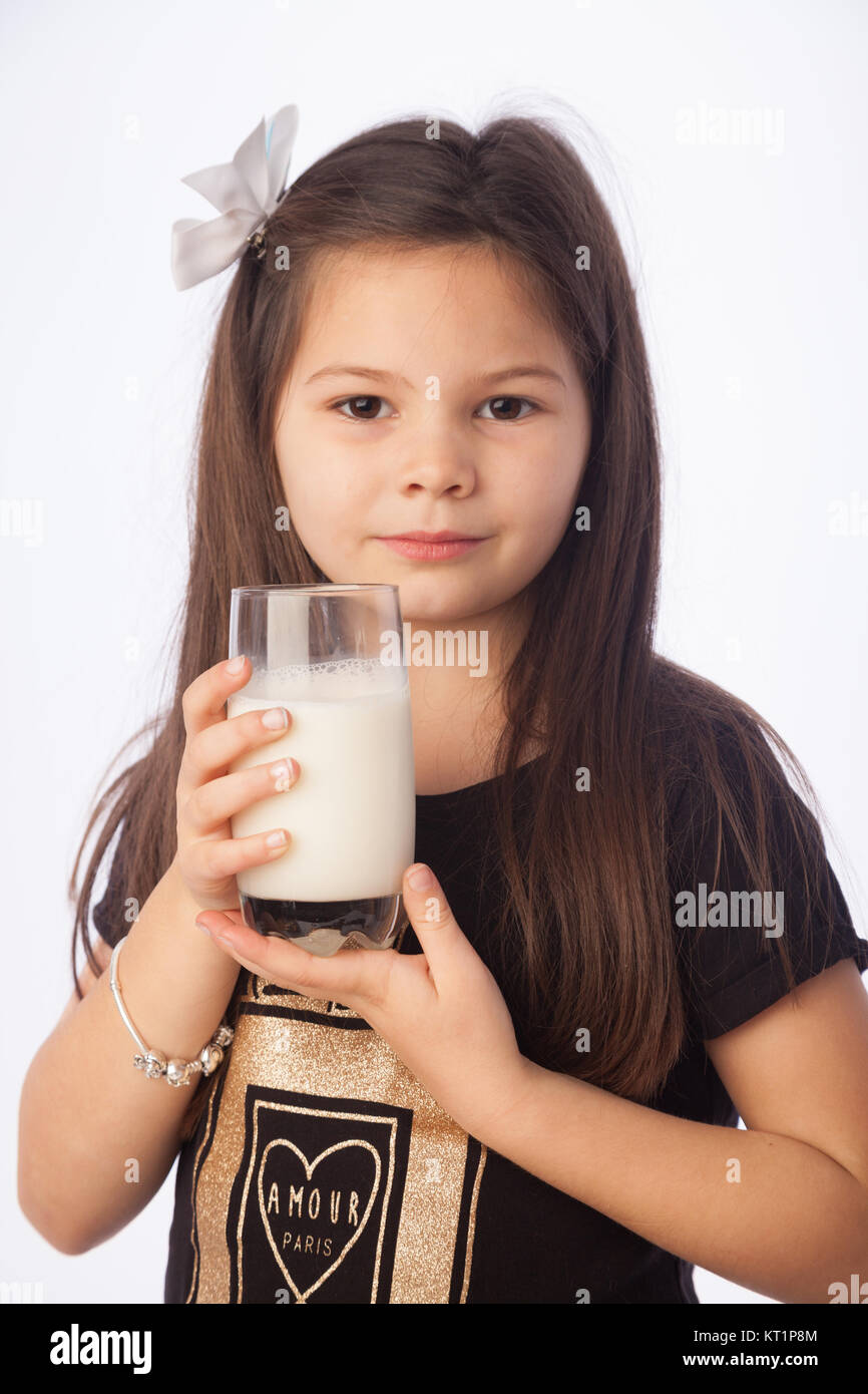 Ein sieben Jahre altes Mädchen hält ein Glas Milch, süß mit Milch Schnurrbart. Stockfoto