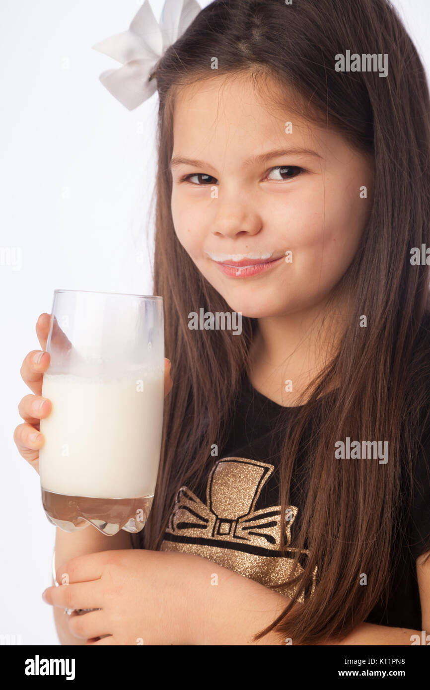 Ein sieben Jahre altes Mädchen hält ein Glas Milch, süß mit Milch Schnurrbart. Stockfoto
