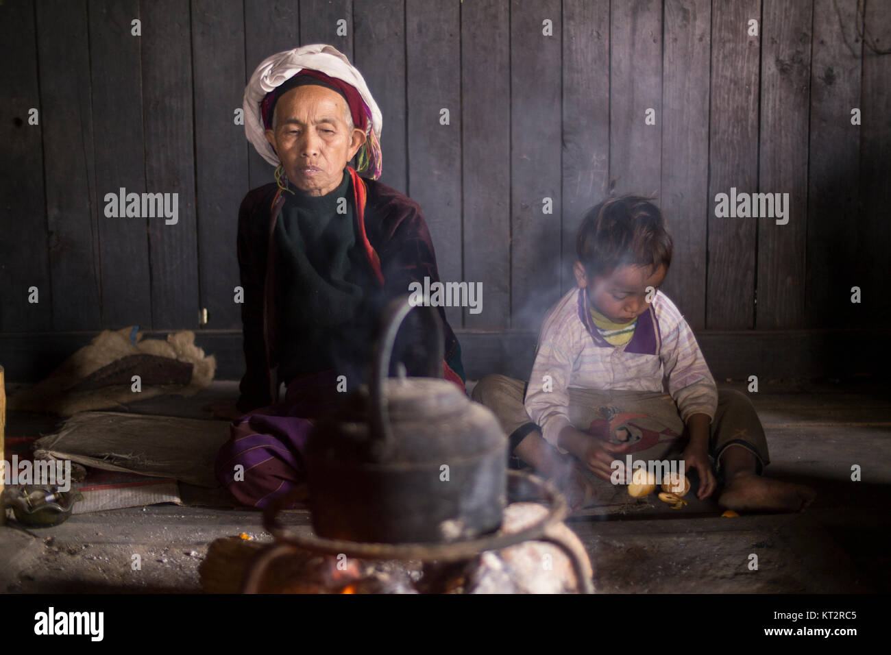 Ein älterer Palaung Frau trägt eine bunte ethnische Kostüm sitzt am Feuer neben einem jungen kleinen Jungen in ihr Haus im Dorf. Stockfoto