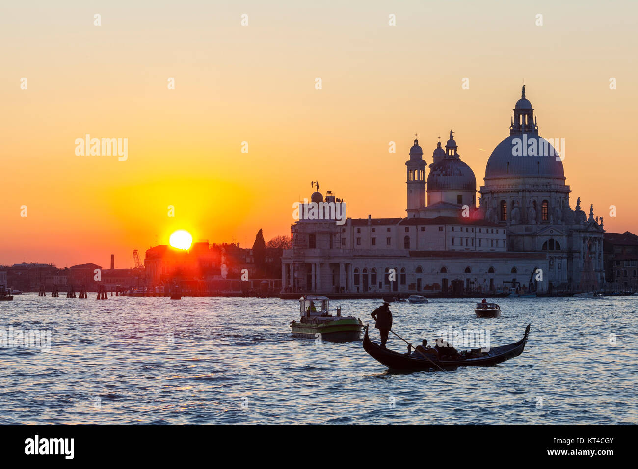 Bunte orange Sonnenuntergang über der Lagune von Venedig und der Basilika di Santa Maria della Salute mit Booten und einer Gondel im Vordergrund, lens flare Stockfoto