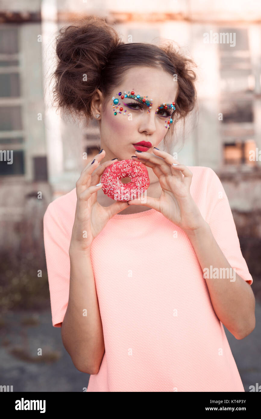 Beauty fashion model Mädchen nehmen bunte Donuts. Lustige fröhliche Frau mit Süßigkeiten, Dessert. Diät, Diät Konzept. Junk Food, Abnehmen, Gewichtsverlust. Modische Mädchen mit kreativen Make-up und Donut Stockfoto