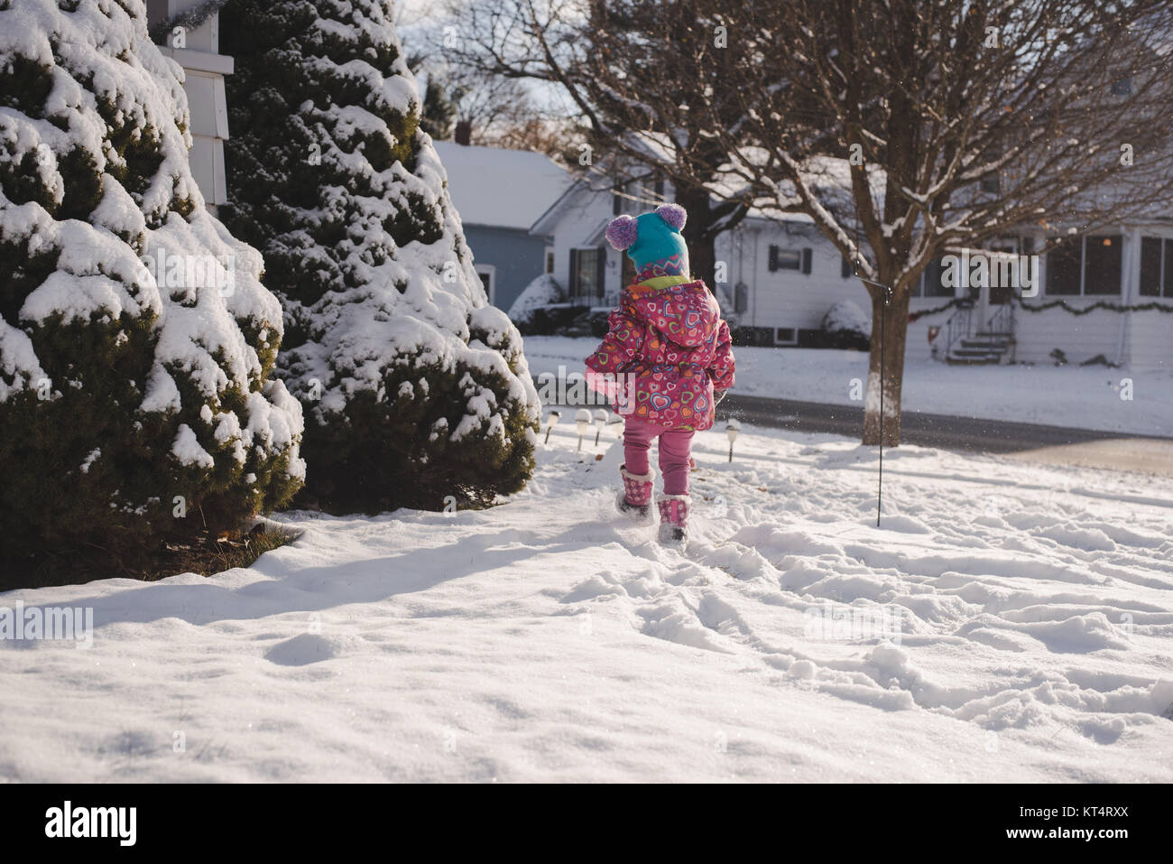Ein Kleinkind Mädchen mit einem bunten Mantel spielt im Schnee. Stockfoto