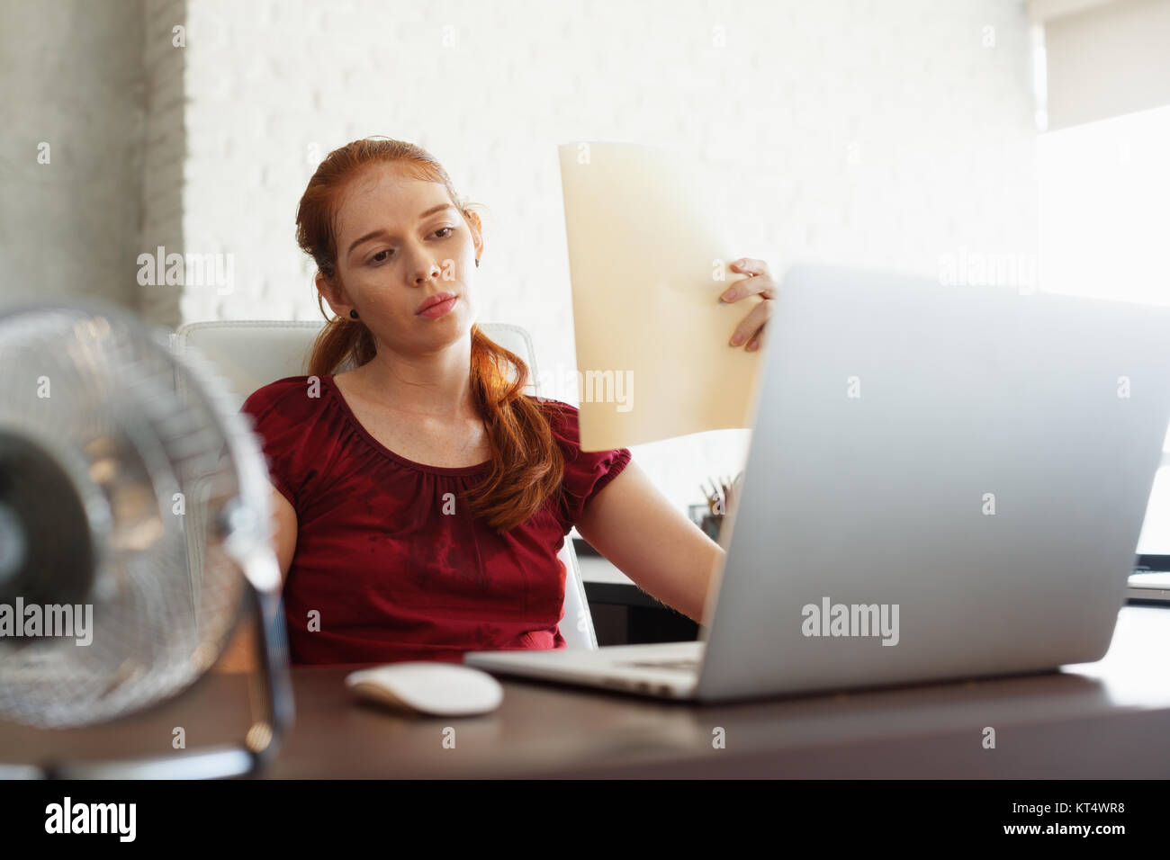 Portrait der junge rothaarige Frau arbeiten mit Computer Laptop im Büro im Sommer während der Hitzewelle. Die Temperatur ist heiß und das Haar Conditioner wird b Stockfoto