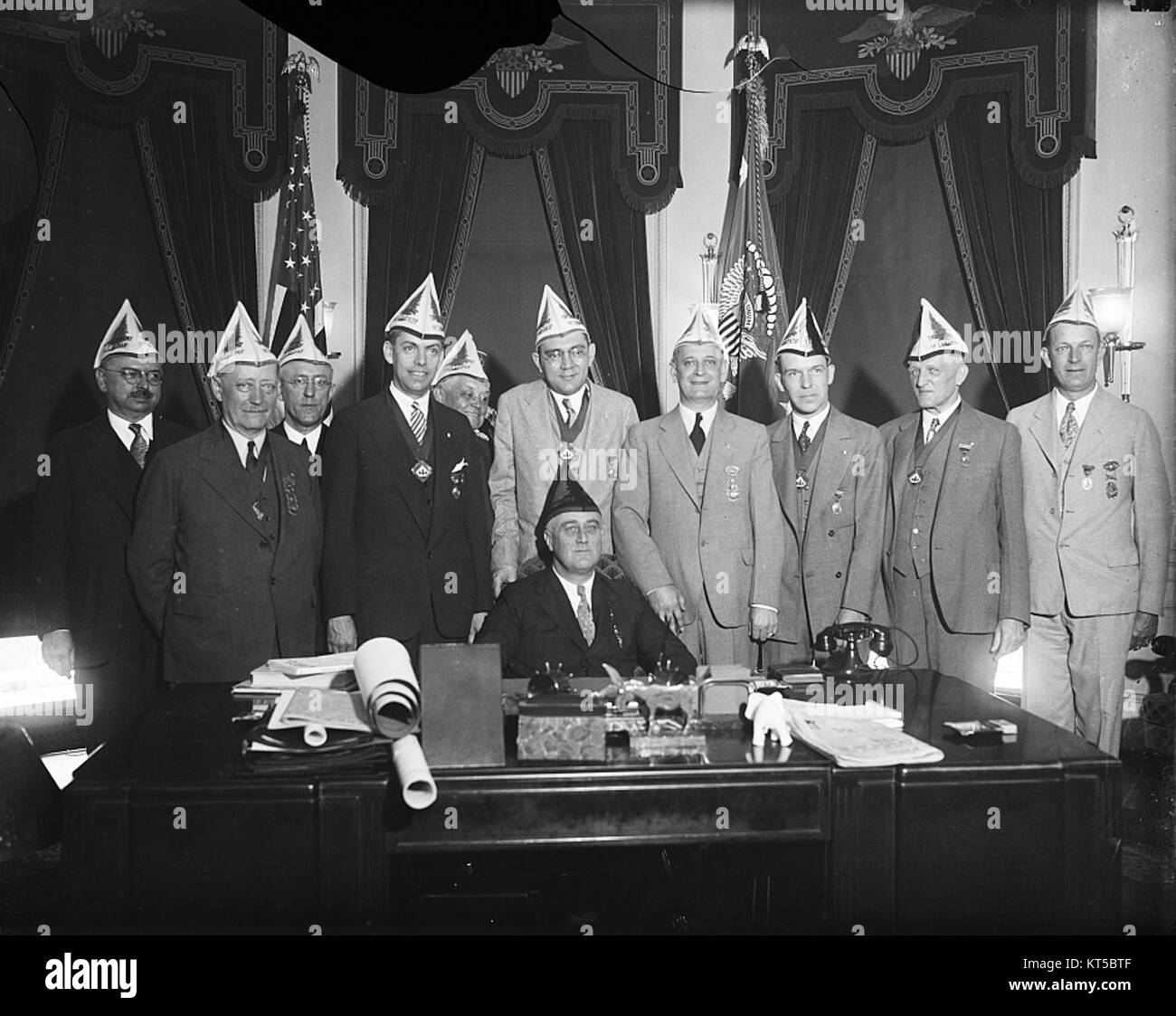 Dieses Foto zeigt Präsident Franklin D. Roosevelt mit einer Gruppe von Einzelpersonen, wahrscheinlich von einem bedeutenden politischen oder historischen Ereignis. Roosevelt, bekannt für seine Führungsrolle während der Weltwirtschaftskrise und des Zweiten Weltkriegs, bleibt eine zentrale Figur in der amerikanischen Geschichte. Stockfoto