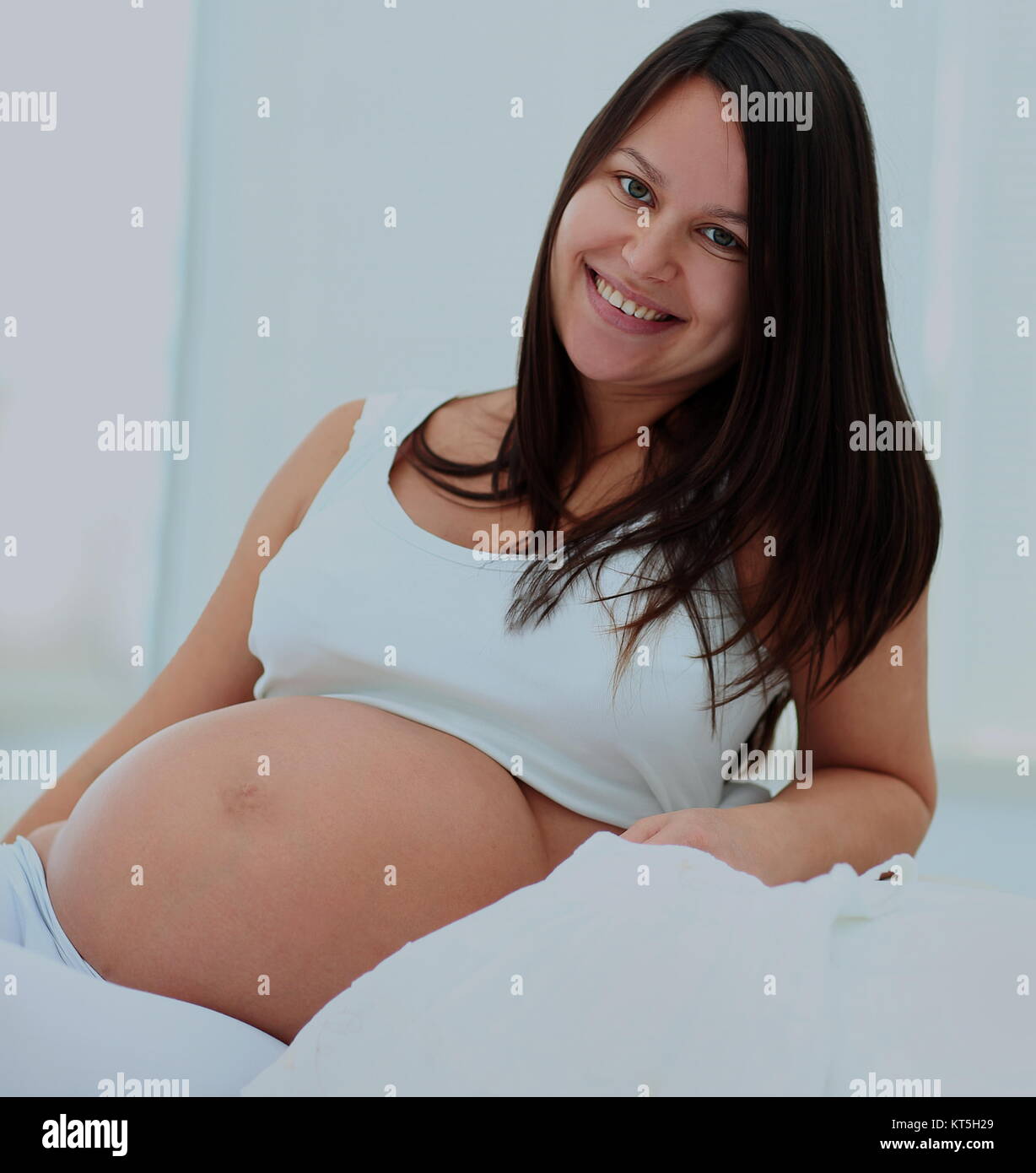 Glückliche Schwangerschaft sitzt auf dem Sofa zu Hause im Schlafzimmer Stockfoto