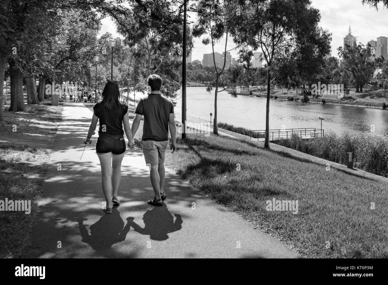 Schwarz-weiß Foto von einem jungen Paar, Hände halten, wandern von der Kamera entfernt, am Fluss Pfad, an einem Sommernachmittag in Melbourne, Australien Stockfoto