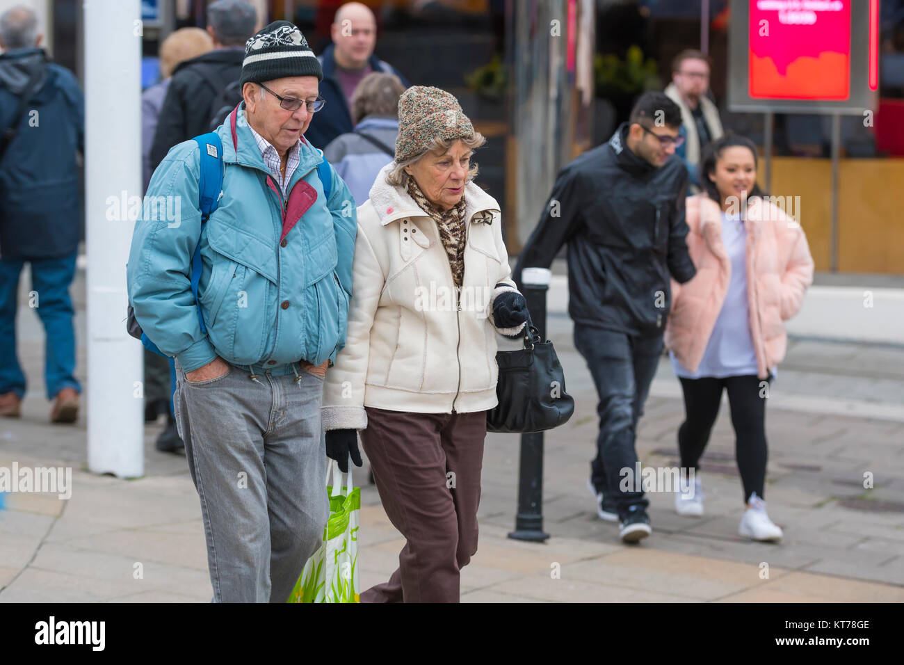 Senior Paar, man läuft durch eine Stadt einkaufen, in Hut und Mantel im Winter in Großbritannien gekleidet. Stockfoto