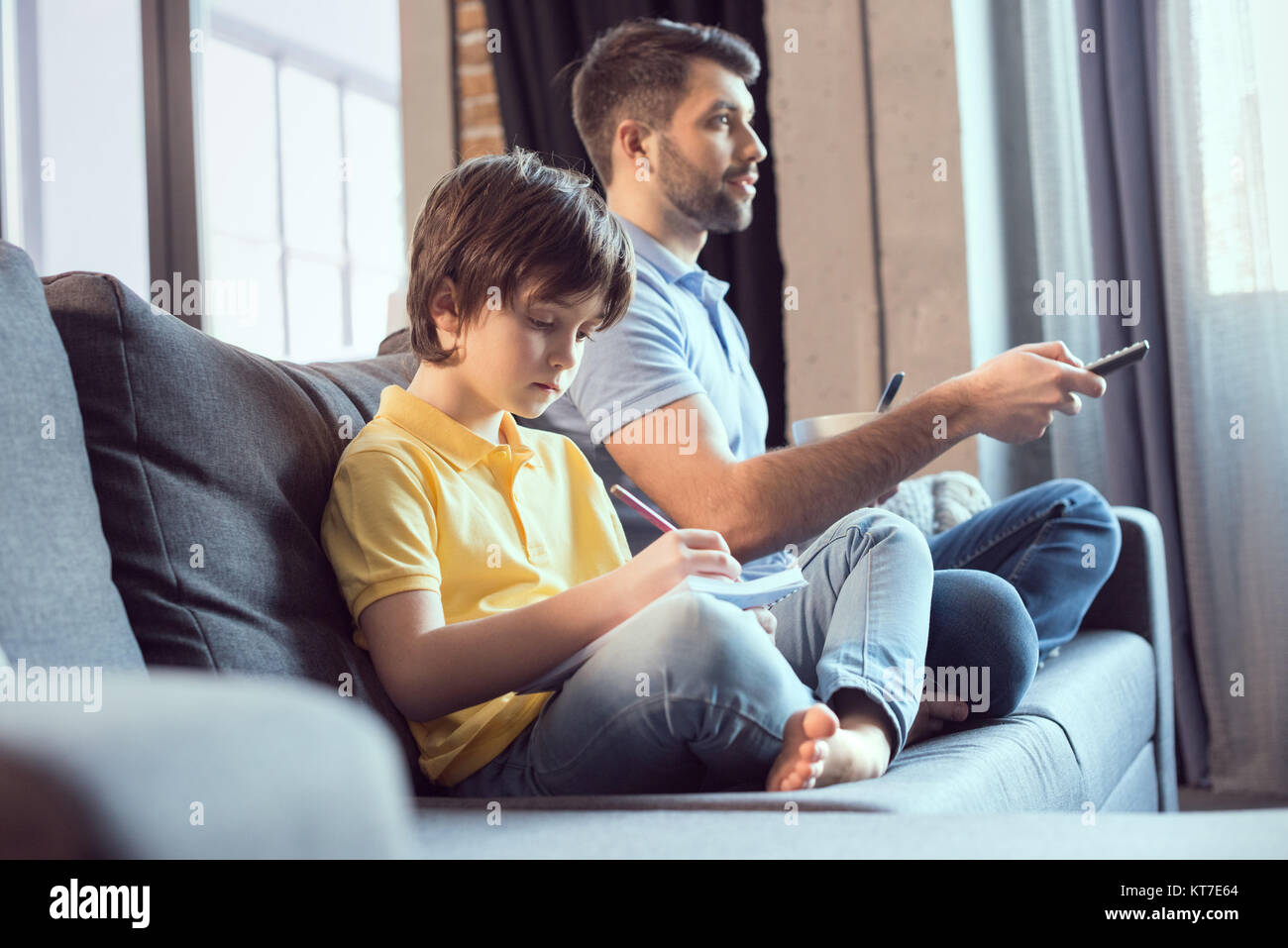 Vater aufzupassen Film und Essen Frühstück, während Sohn Hausaufgaben Stockfoto