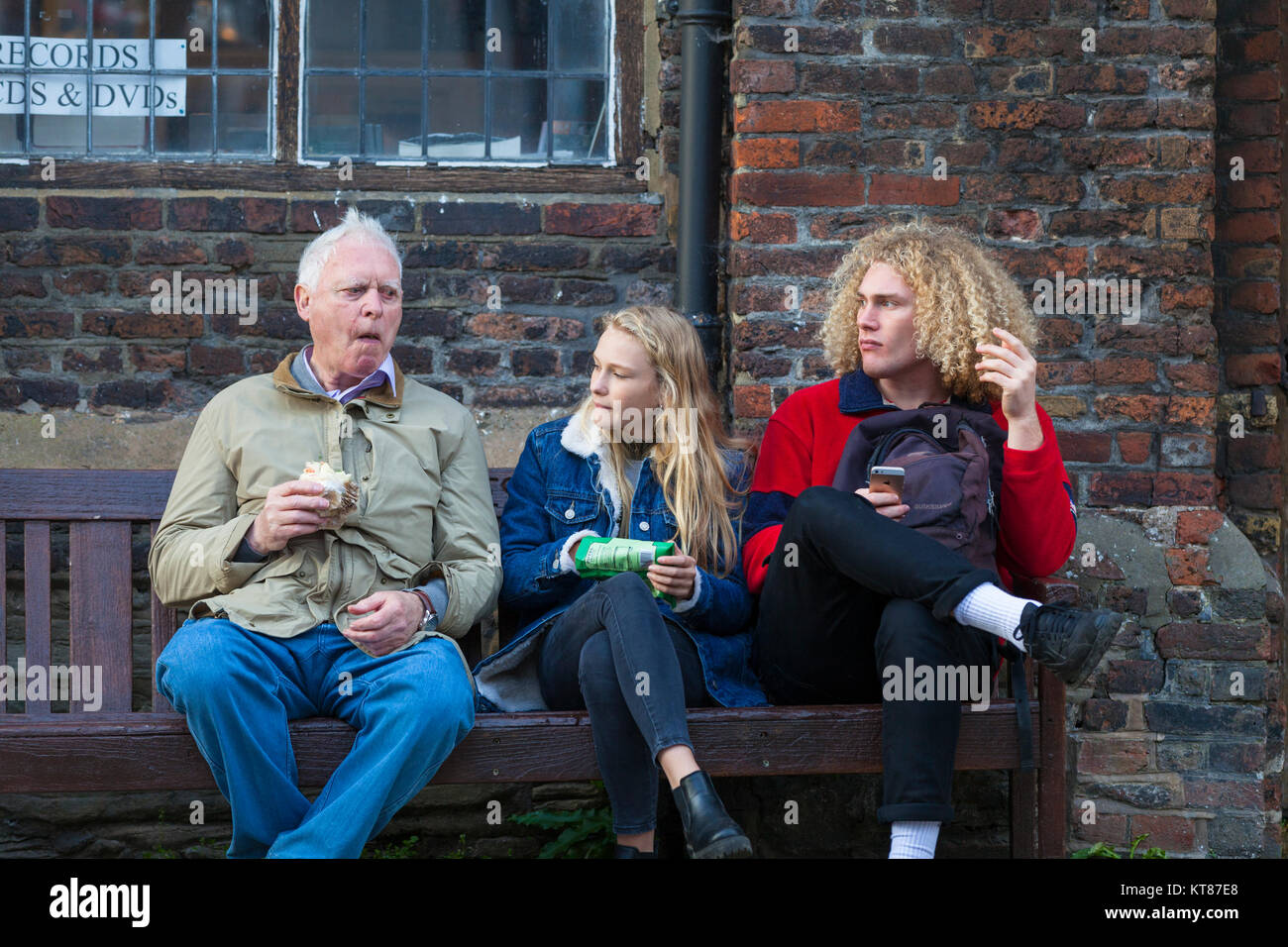 Menschen, die auf einer Bank sitzen Essen außerhalb einem alten Backsteingebäude, Roggen East Sussex Stockfoto