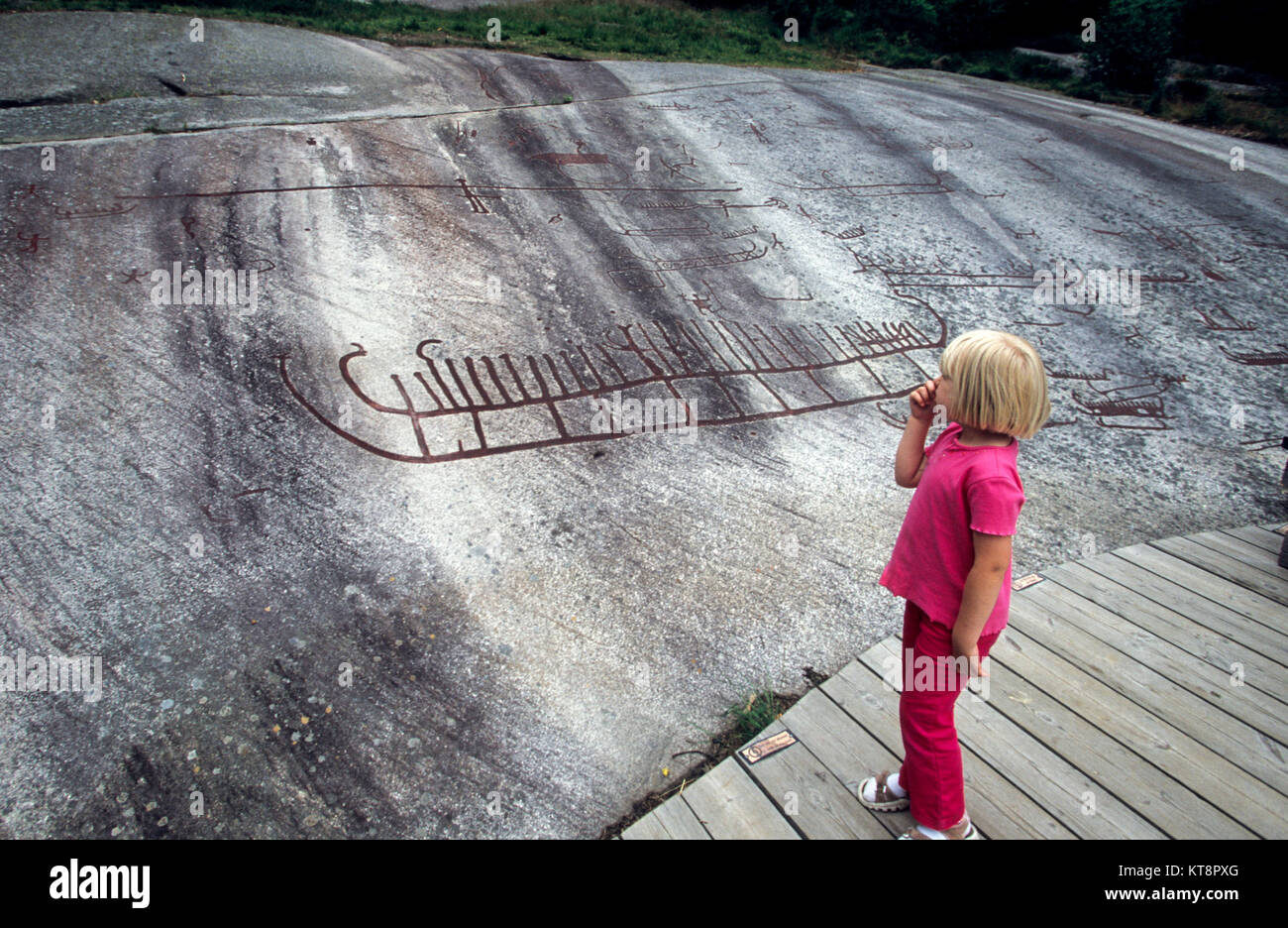 Junge Mädchen saugt die Daumen und schaut auf die Schnitzereien in Tanum Bohulslän 2010 Stockfoto