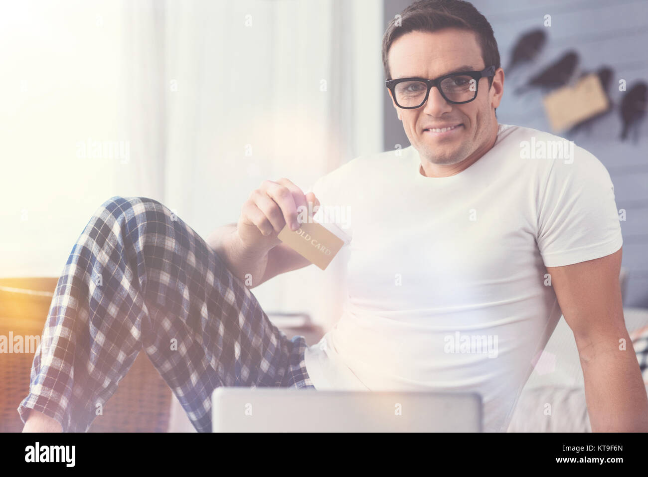 Kaufen Formular home. Positive attraktiver Mann mit einer Kreditkarte für die Bezahlung seiner erwerben, während der Morgen mit seinem Laptop begeistert Stockfoto