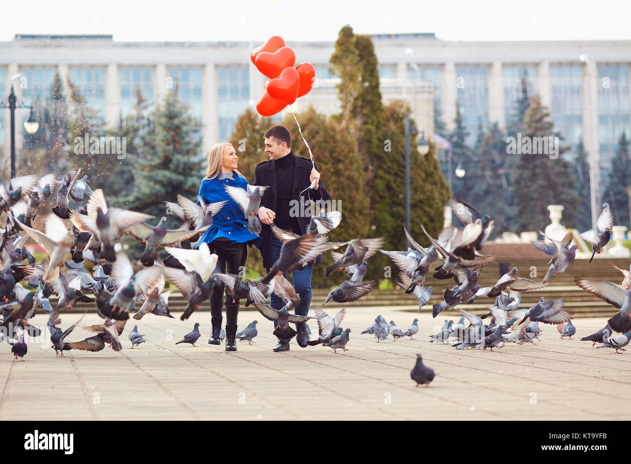 Ein liebevolles Paar in einem Mantel mit Ballons der Herzen in die Hände läuft mit Tauben auf der Straße der Stadt. Valentinstag. Stockfoto