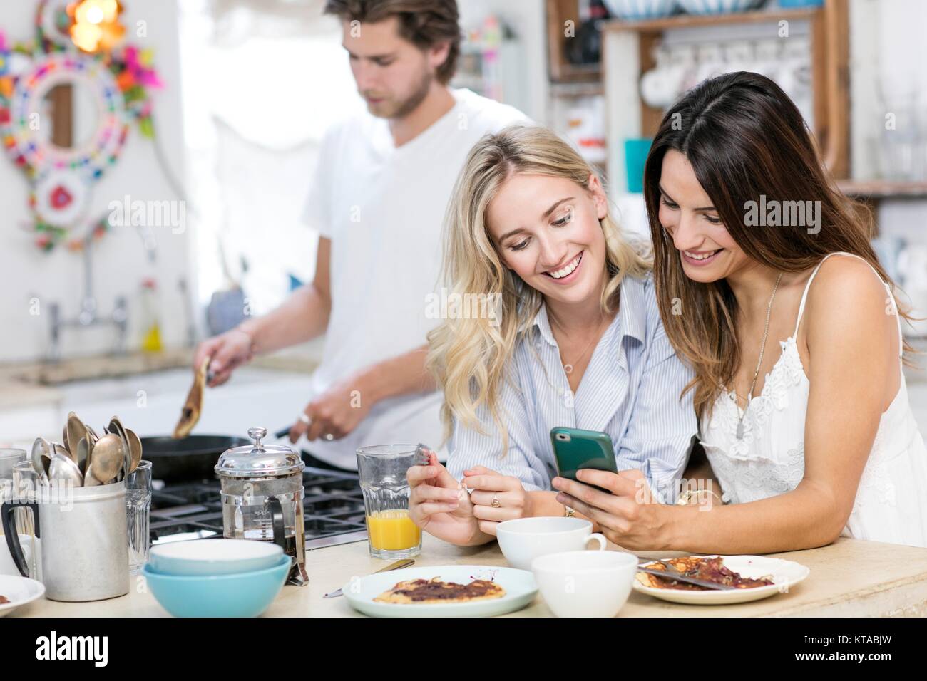 Junge Frauen, die am Smartphone in der Küche mit dem Frühstück. Stockfoto