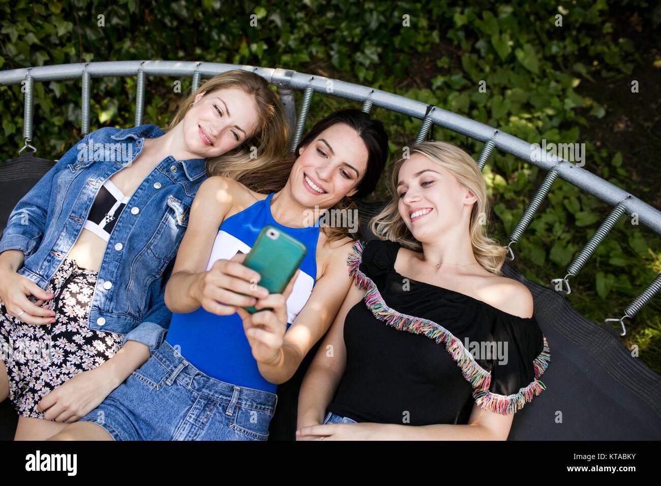 Drei junge Frauen liegen auf Trampolin mit Smartphone. Stockfoto