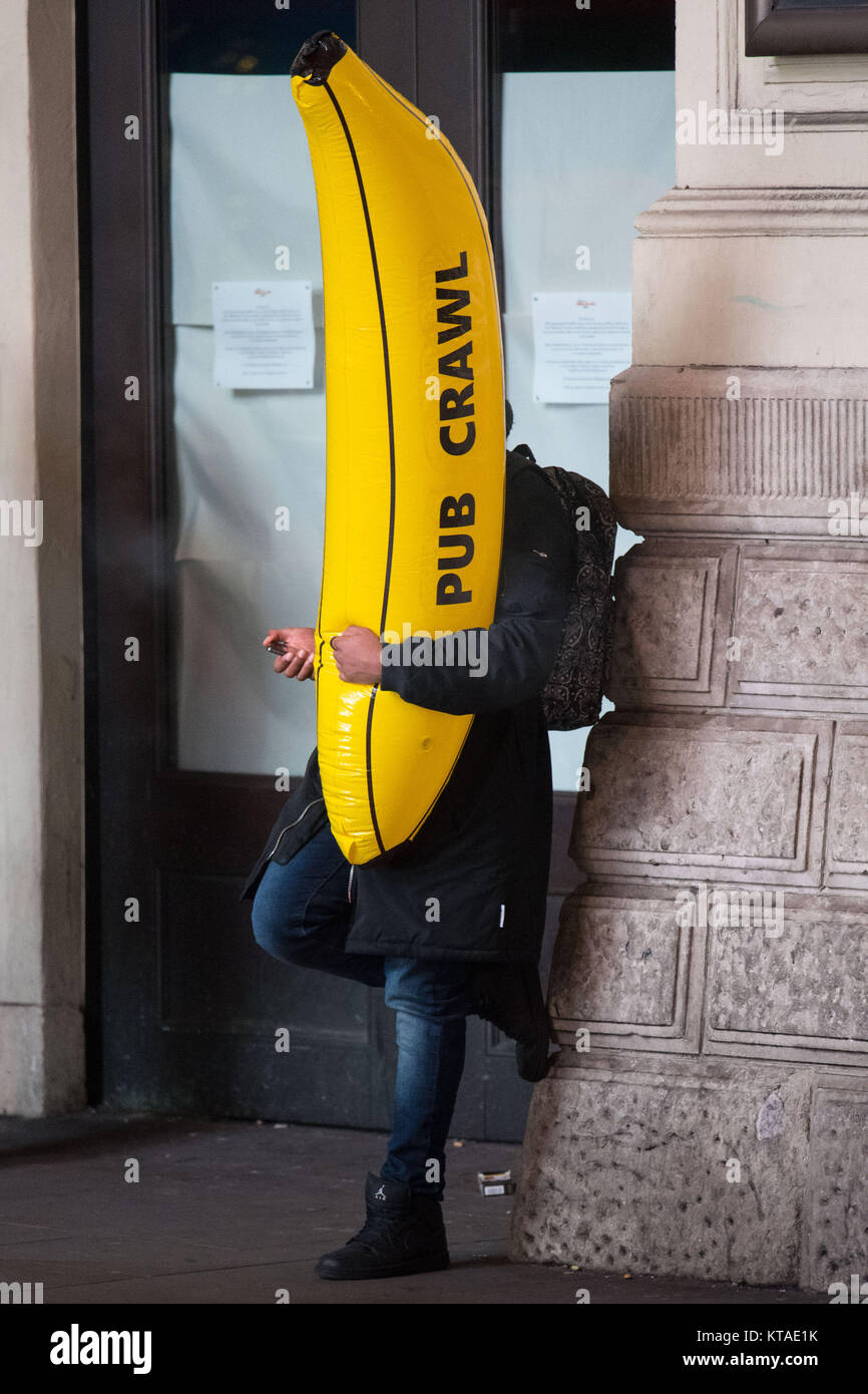 Ein Nachtschwärmer hält eine aufblasbare Banane, während er am „Black Eye Friday“ oder „Mad Friday“ in London unterwegs ist, während die Menschen im ganzen Land den Beginn der Weihnachtspause mit Bars, Pubs und Clubs feiern. Stockfoto