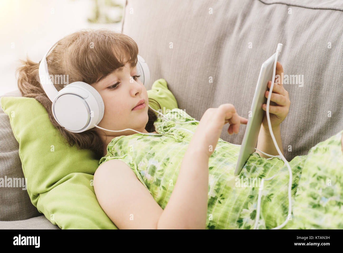 Süße Mädchen auf dem Sofa entspannen und mit einem digitalen Tablet, sie trägt Kopfhörer und Apps Stockfoto