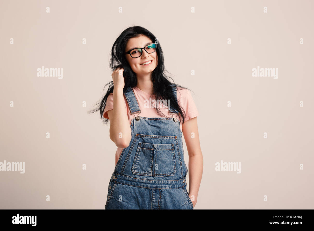 Schöne smiling brunette Mädchen Tragen einer Brille in Denim insgesamt Neben leere Wand posieren Stockfoto