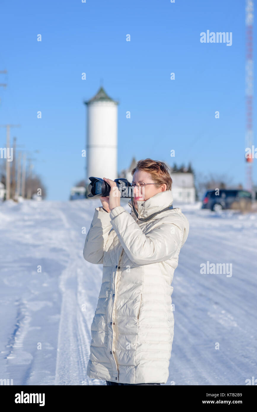 Im Vordergrund steht eine junge Frau mit Brille, im Winter im weißen Kittel Fotografien, auf der Rückseite eines verschwommenen Plan, einem Land Straße im Schnee, ein wh Stockfoto
