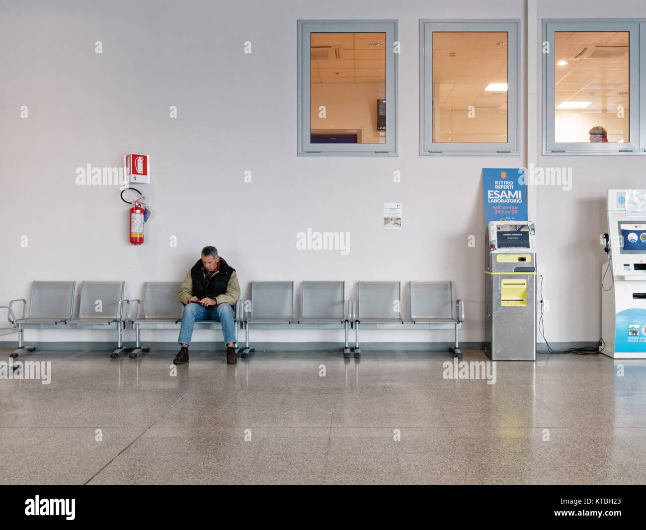 Biella, Italia - Dezember 15, 2017: einzelner Mann wartet, sitzt im Atrium der Biella Krankenhaus nahe der Bericht Maschinen. Real-life Moment, während Sie Stockfoto