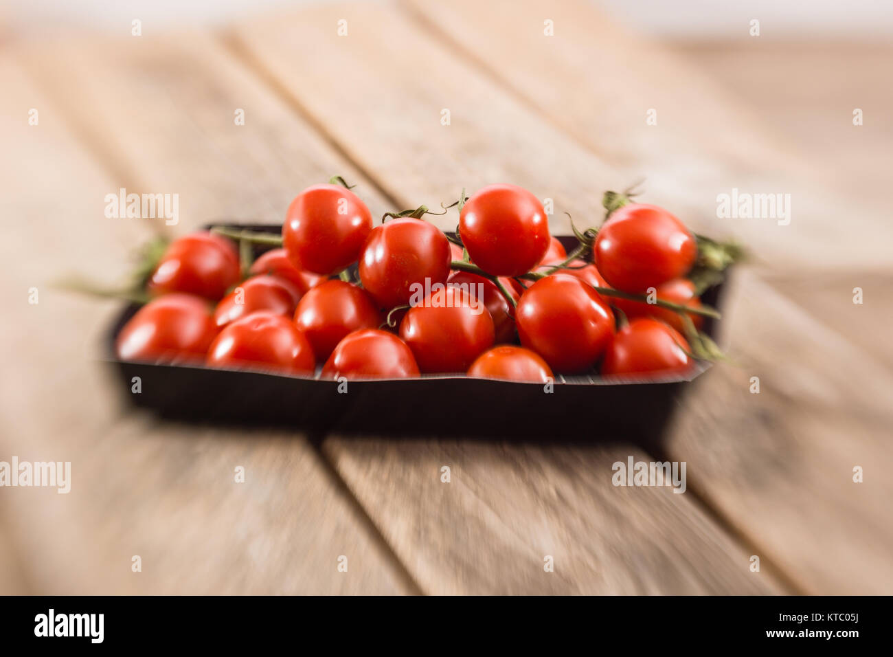 Kleine Rispentomaten in einer Schale auf einem Holzbrett Stockfoto