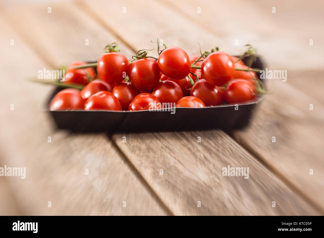 Kleine Rispentomaten in einer Schale auf einem Holzbrett Stockfoto