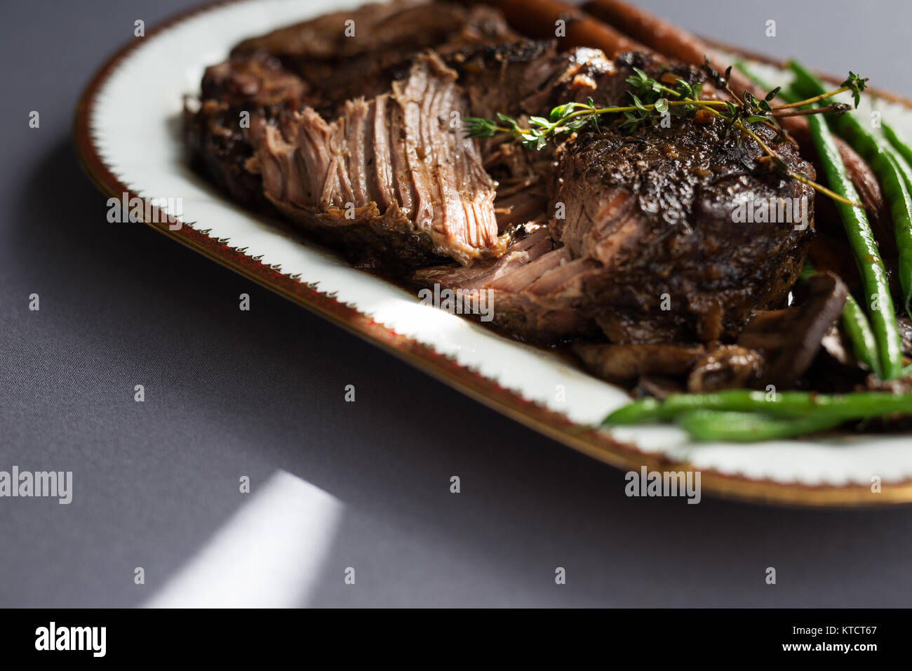 Langsam gekochtes Rindfleisch Schmorfleisch mit grünen Bohnen, Karotten und Pilze auf einem weißen Teller. Grau Tischdecke, Thymian garnieren. Kopieren Sie Platz. Stockfoto