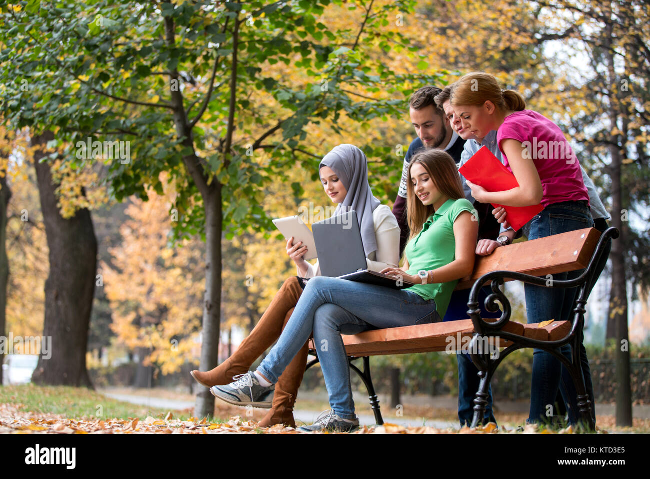 Gruppe von Jugendlichen mit Notebook und Tablet-PC auf einer Parkbank, Spass haben, Reden, heraus hängen Stockfoto