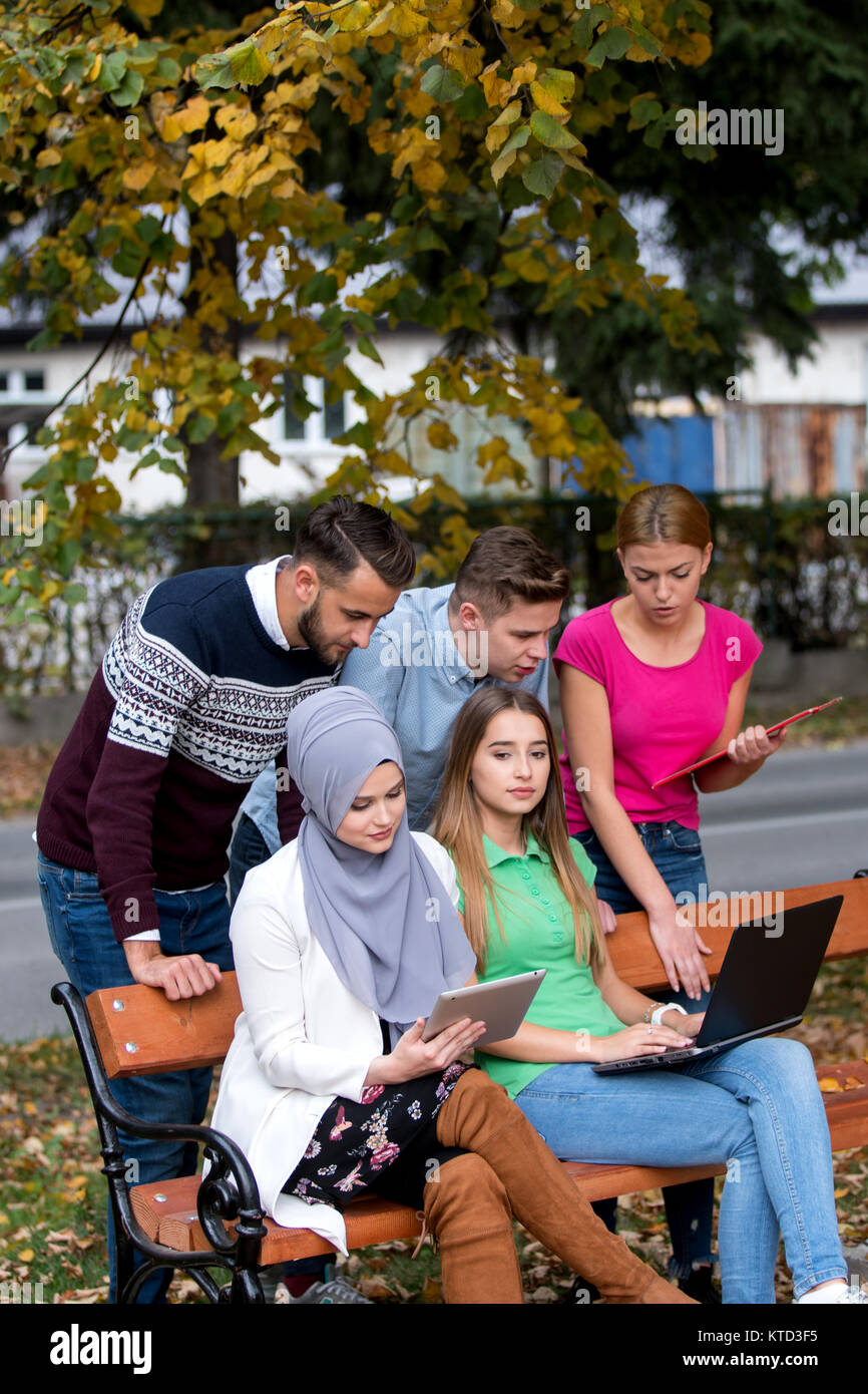 Gruppe von Jugendlichen mit Notebook und Tablet-PC auf einer Parkbank, Spass haben, Reden, heraus hängen Stockfoto