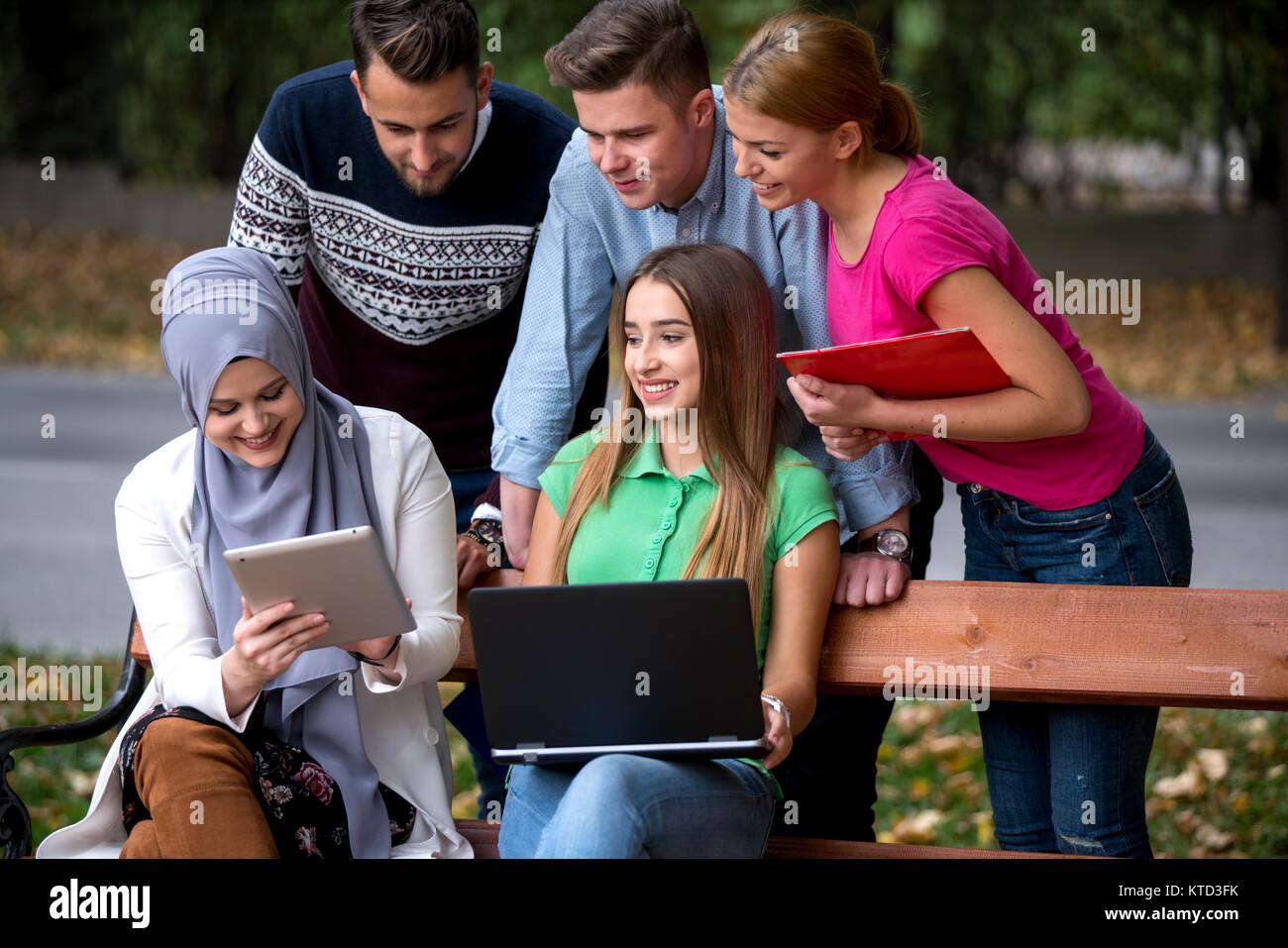 Gruppe von Jugendlichen mit Notebook und Tablet-PC auf einer Parkbank, Spass haben, Reden, heraus hängen Stockfoto