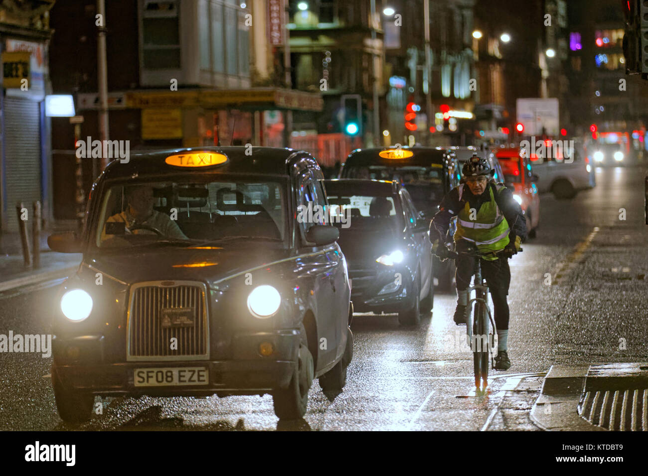 Schwarze Taxis spät in der Nacht in der Straße Straße mit männlich Mann Radfahrer auf dem Fahrrad Raum nahe bei anderen Taxis in einer Linie der Verkehr Stockfoto