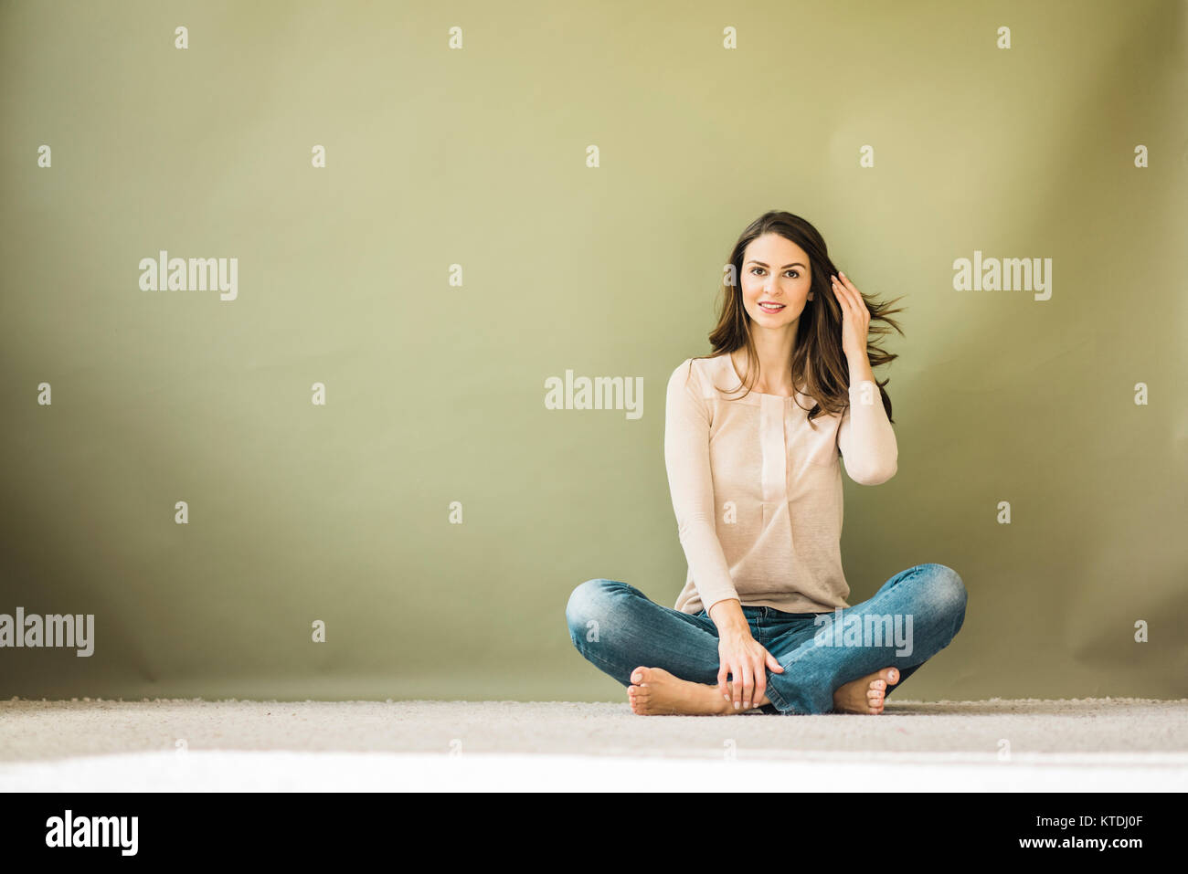 Portrait von Frau sitzt auf dem Boden vor grünem Hintergrund Stockfoto