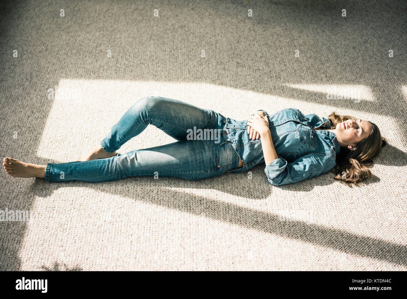 Junge Frau liegt auf dem Teppich im Wohnzimmer Sonnenlicht genießen. Stockfoto