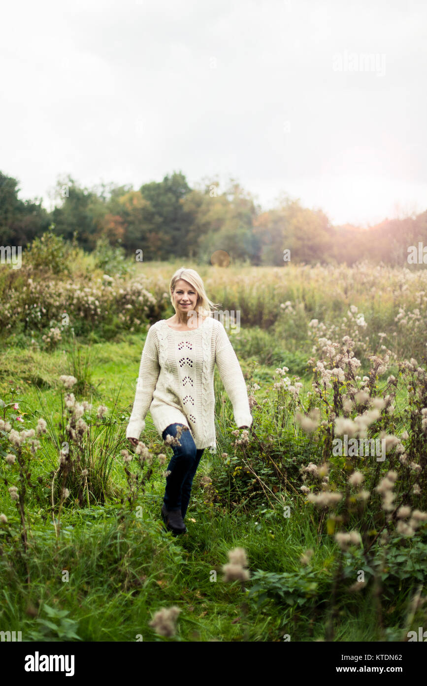 Lächelnde blonde Frau zu Fuß in der Natur Stockfoto