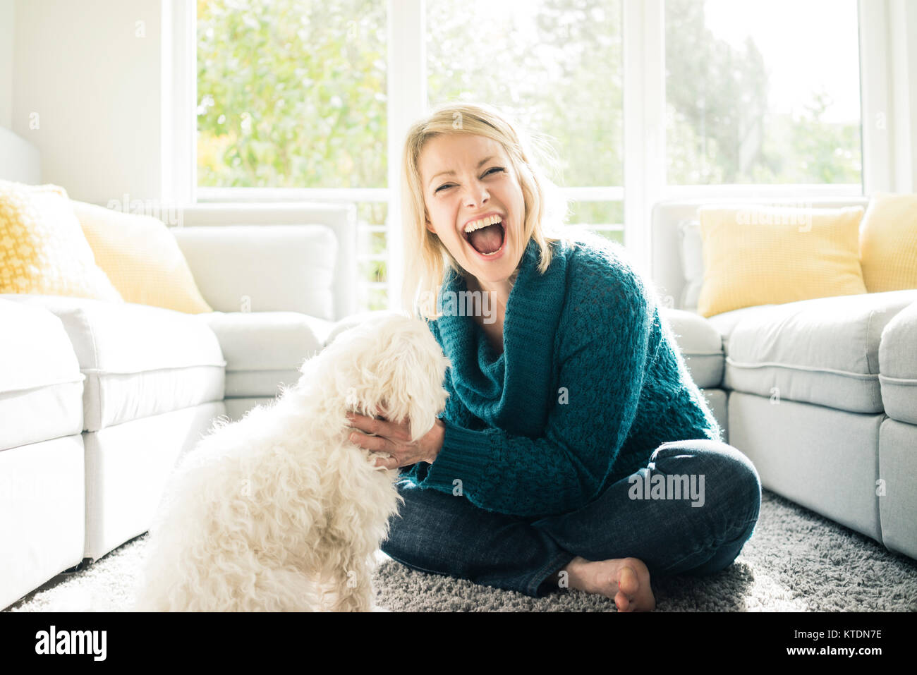 Verspielte Frau mit ihrem Hund im Wohnzimmer Stockfoto