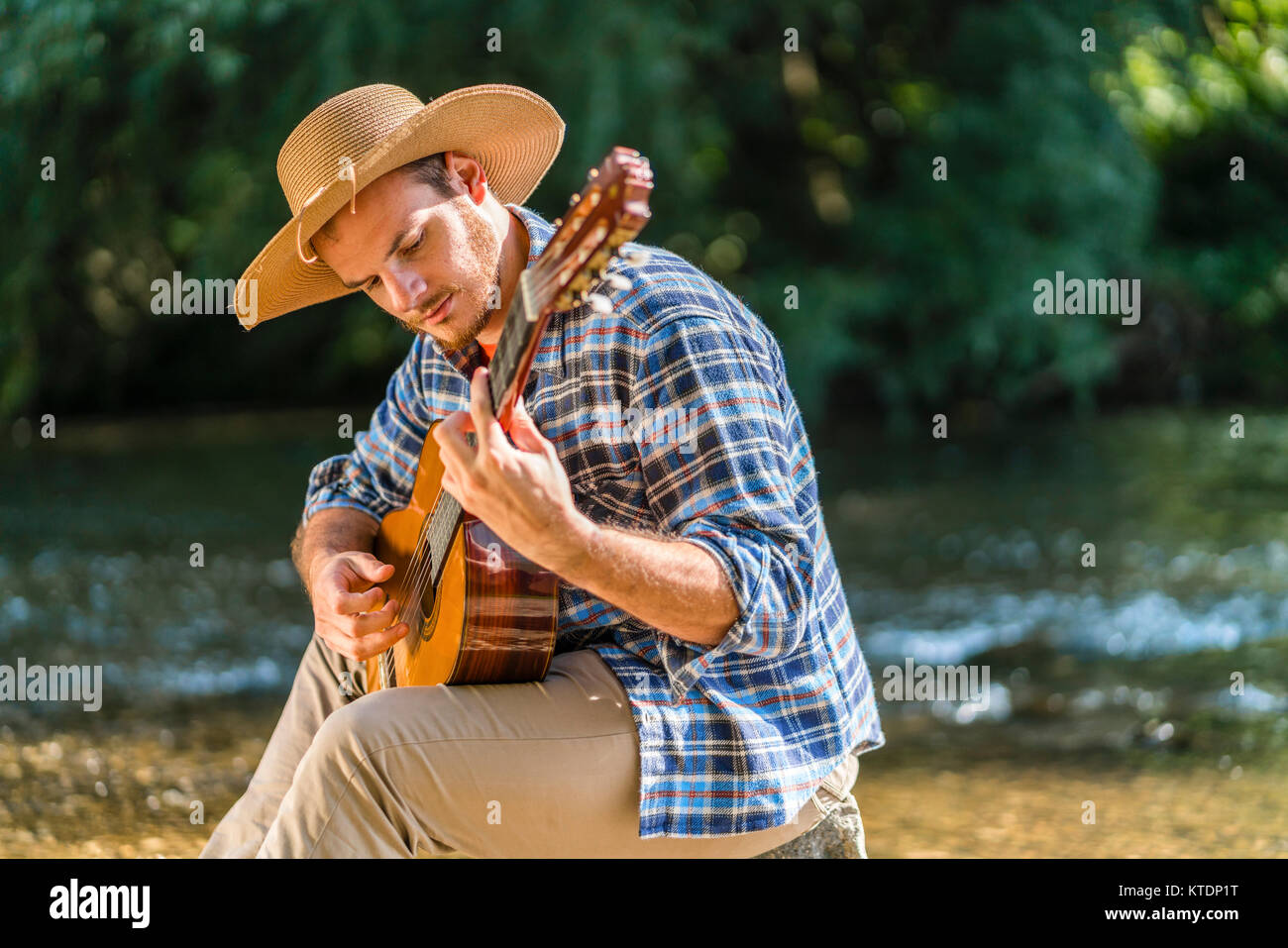 Mann spielt Gitarre am Flußufer Stockfoto
