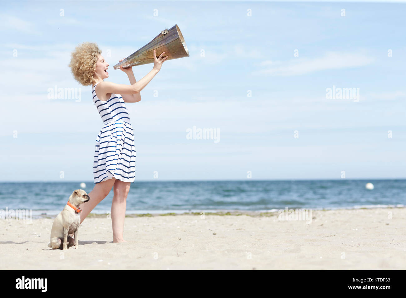 Junge Frau mit Megafon und Hund am Strand Stockfoto