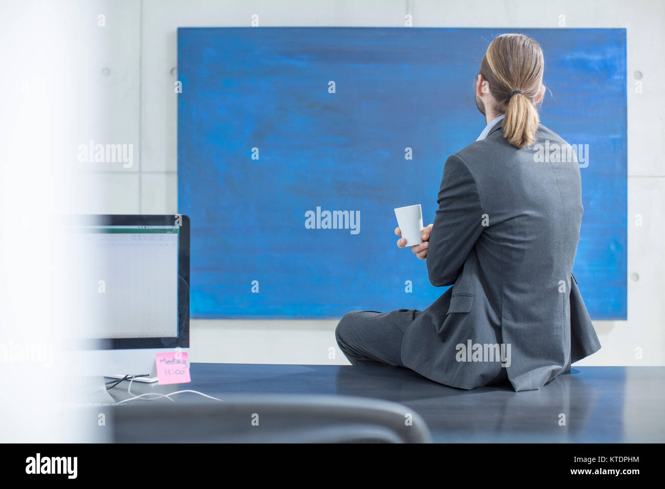 Unternehmer im Büro zu sitzen am Schreibtisch an einem blauen Malerei suchen Stockfoto